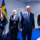 NATO Secretary General Jens Stoltenberg with his hand out, Turkish President Tayyip Erdogan, and three other people, all looking off camera and wearing suits. Various flags are against the wall of what appears to be a conference room with a very blue floor.